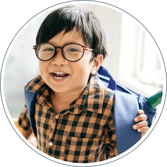 Child wearing glasses smiling indoors with backpack