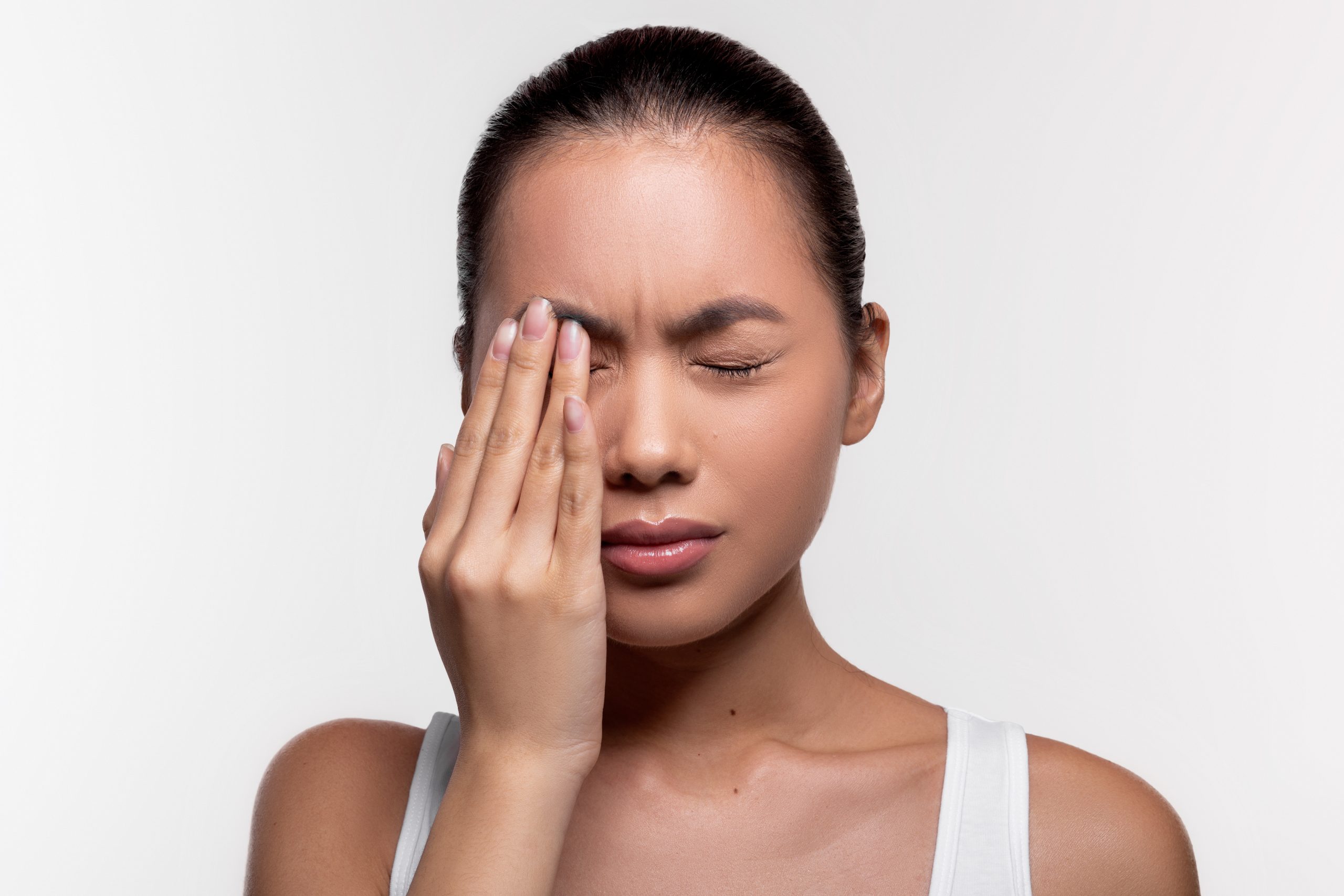 Upset young asian woman suffering from strong eye pain, touching her eye and crying over white studio background, closeup photo, copy space. Healthcare, eye disorders and diseases concept